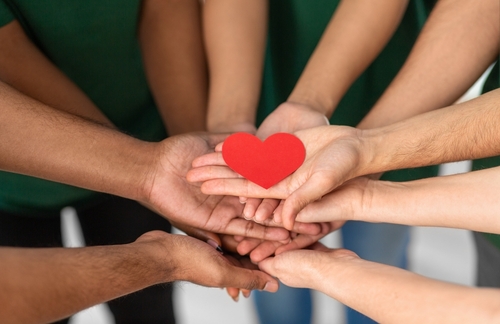 charity_ support and volunteering concept - close up of volunteers s hands holding red heart at distribution or refugee assistance center